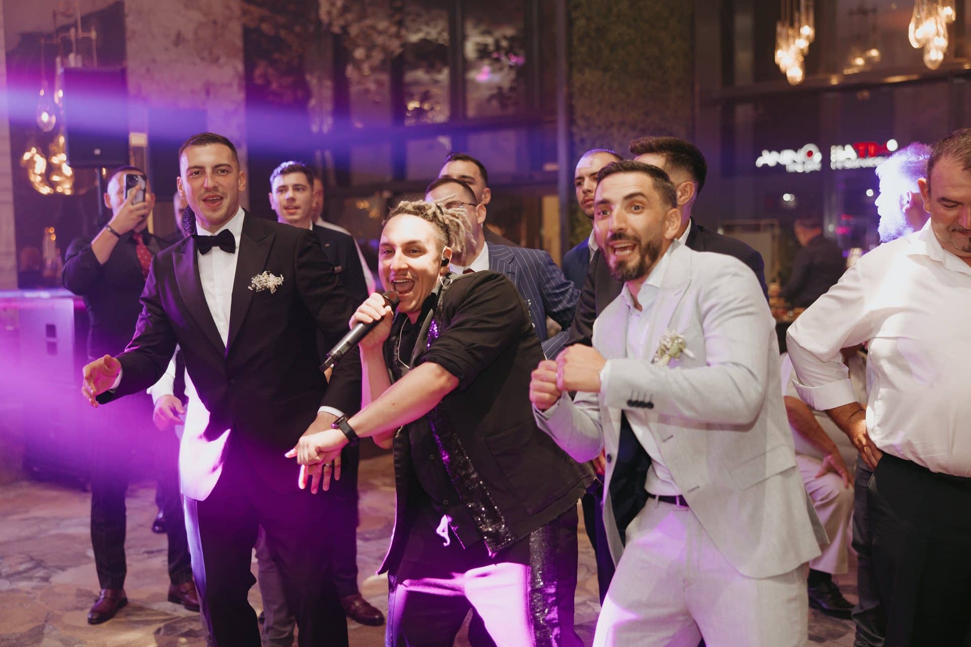 Solistul trupei dansează cu mirele și invitații, în lumini violet