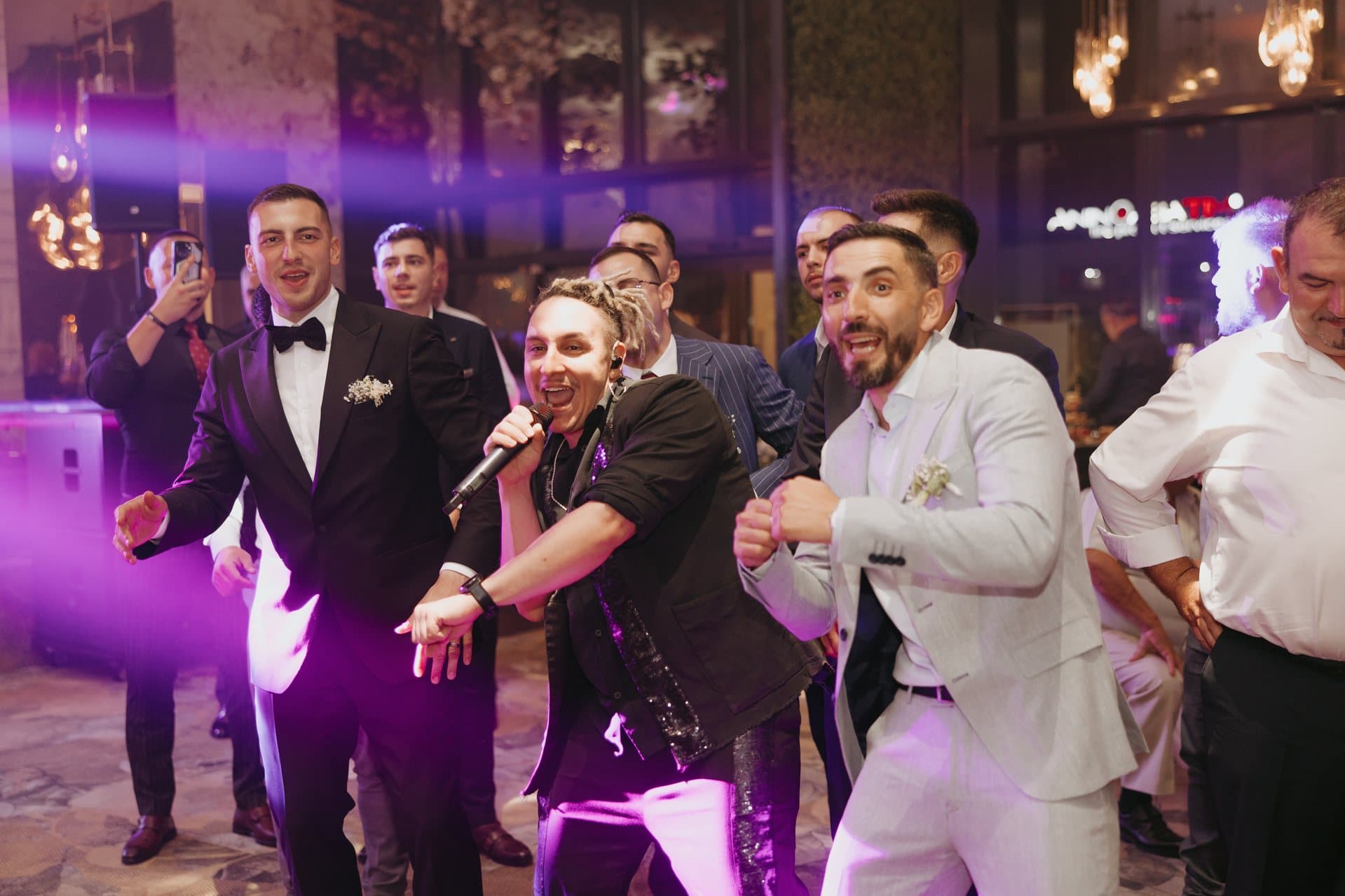 Solistul trupei dansează cu mirele și invitații, în lumini violet